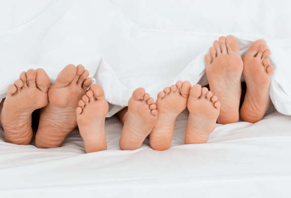 Family feet resting under white bedding, representing healthy feet and everyday footcare